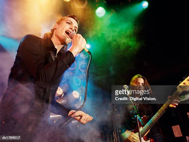 male singer and guitarist in an indie band perform on smoky, spotlit stage - pop music instruments stock pictures, royalty-free photos & images