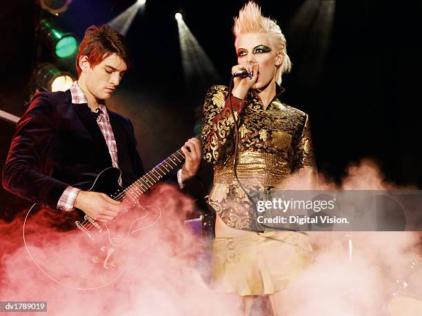 female rock band singer with a gold mini-skirt and blond quiff and a male guitarist perform on a smoky stage - blonde female singers stock-fotos und bilder