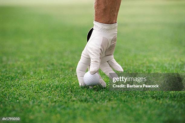 hand putting golf ball on a tee - green glove stock pictures, royalty-free photos & images
