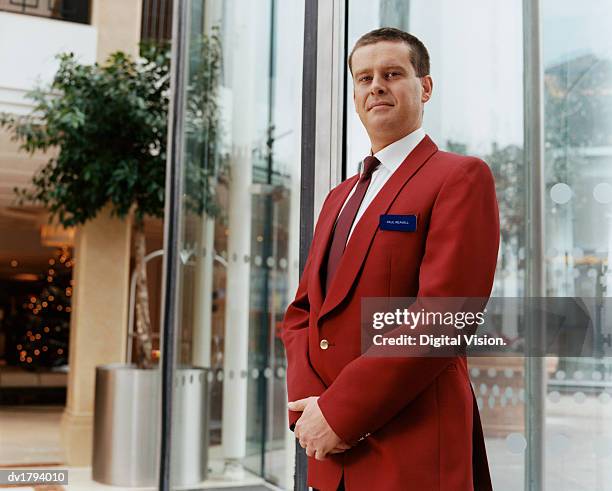 portrait of a hotel doorman in a smart red jacket, standing in a lobby by the entrance - smart 個照片及圖片檔