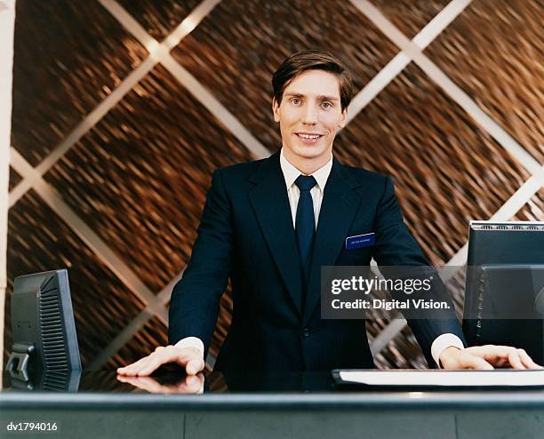 portrait of a male hotel receptionist standing behind a reception desk - boss nameplate stock pictures, royalty-free photos & images