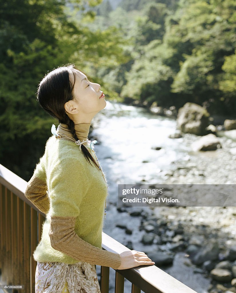 Woman Standing on a Bridge over a River with Her Eyes Closed and Inhaling