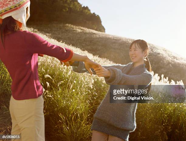 two woman standing face to face and holding hands, at the base of a hill, in a field of long grass - length stock pictures, royalty-free photos & images