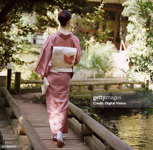 rear view of a woman holding a book and walking on a wooden bridge - kimono foto e immagini stock