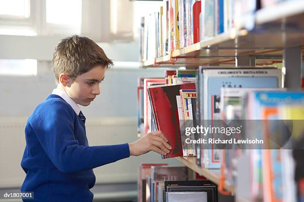 primary school boy in a uniform chooses a book from a shelf in a library - school uniform ストックフォトと画像