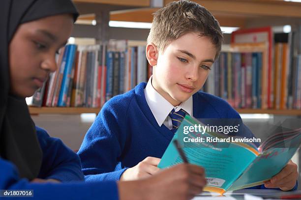 male and female primary school students sit in a library revising, boy reading a math book - anständig klädsel bildbanksfoton och bilder