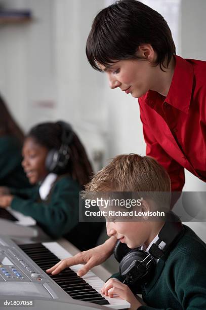 teacher showing a schoolboy how to play an electric piano - how fotografías e imágenes de stock