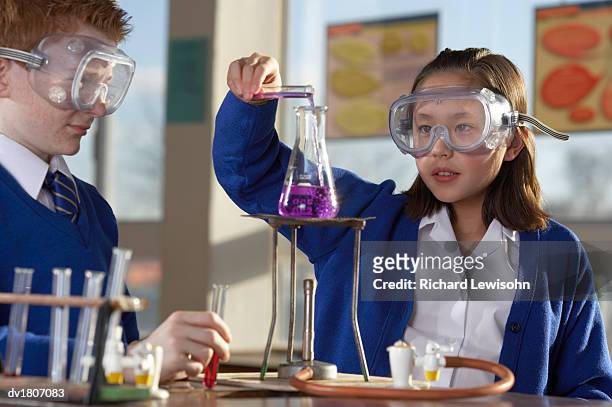 schoolgirl pouring liquid into a science flask watched by a schoolboy - bunsen burner stock pictures, royalty-free photos & images