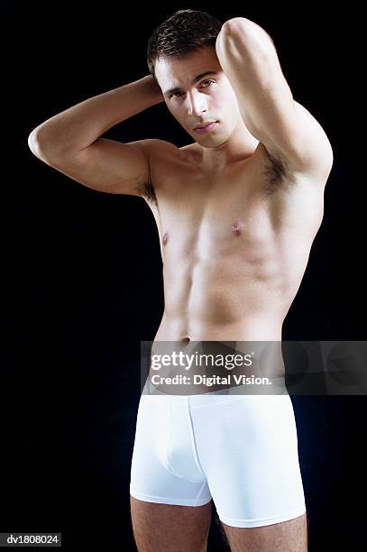 smiling man wearing white boxer shorts stands with his hands behind his head - boxer shorts stock-fotos und bilder