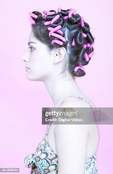 profile of a young woman wearing pink hair curlers - hair curlers stockfoto's en -beelden