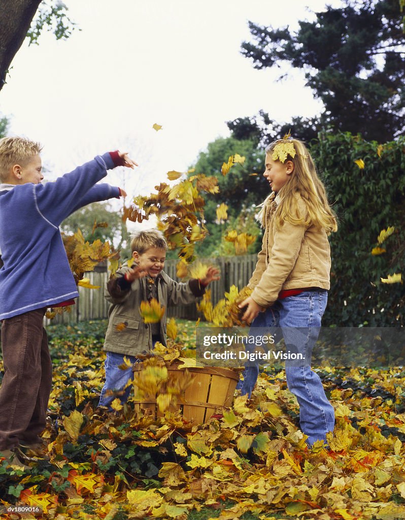 Young Girl and Her Two Brothers Stand in Their Garden Throwing Autumn Leaves From a Basket