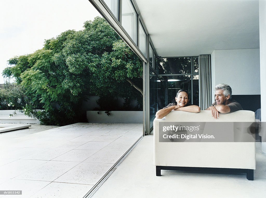 Relaxed Couple Sitting on a Sofa in Their Home With French Windows Open Leading to a Garden