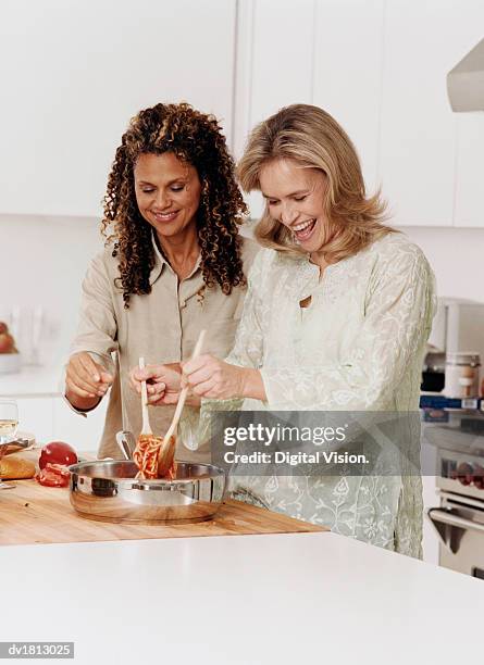 two women standing side by side in kitchen preparing a spaghetti meal - stirring stock pictures, royalty-free photos & images