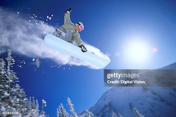 low angle mid air shot of a woman snowboarding - snow board stock pictures, royalty-free photos & images