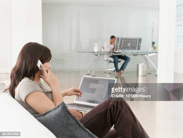 woman sat on a sofa in a modern room, using a mobile phone and a laptop pc - sattel bildbanksfoton och bilder