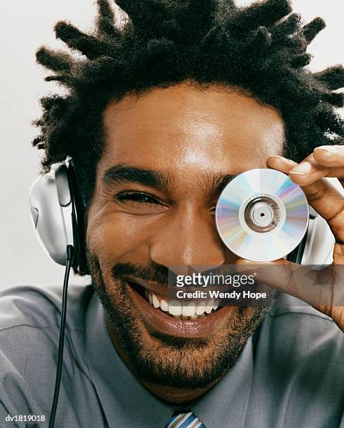 portrait of a smiling man with dreadlocks wearing headphones and holding a compact disk over his eye - hope photos et images de collection