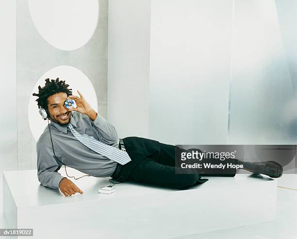 portrait of a man leaning on his elbow and listening to music on headphones while holding a compact disk over his eye - hope photos et images de collection