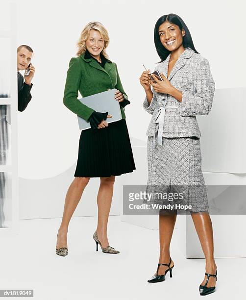 two women holding computers while a man behind them uses a mobile phone - hope photos et images de collection