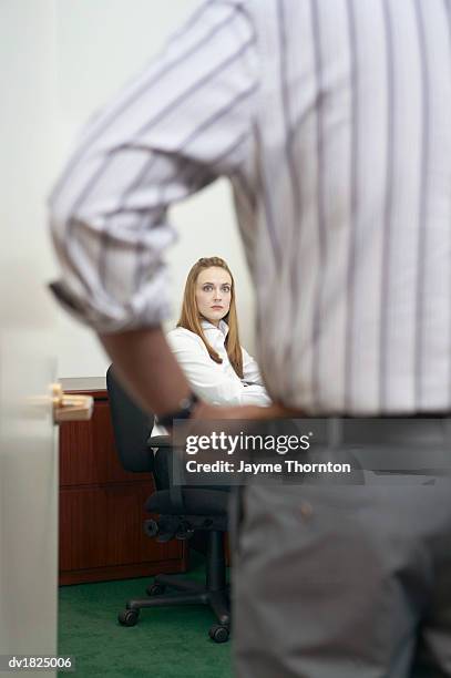 Wide Eyed Businesswoman Sitting At Her Desk Facing Her Manager With His Hands On His Hips, Foto de stock