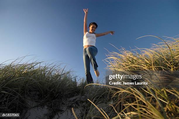 happy woman jumping in the air on a sand dune - happy jumping stockfoto's en -beelden