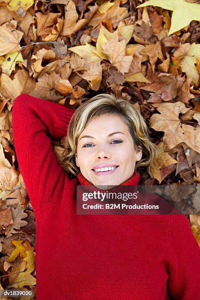 woman wearing a red woolen polo neck jumper lying in autumn leaves - polo neck stock-fotos und bilder