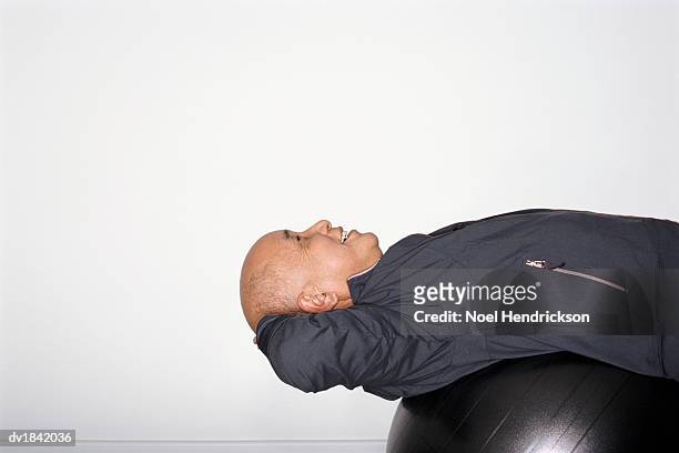 senior man wearing a blue tracksuit top stretching on a fitness ball - tracksuit jacket stock pictures, royalty-free photos & images