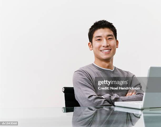 studio shot of a young man sitting at a table with a laptop computer - laptop studio shot stock pictures, royalty-free photos & images