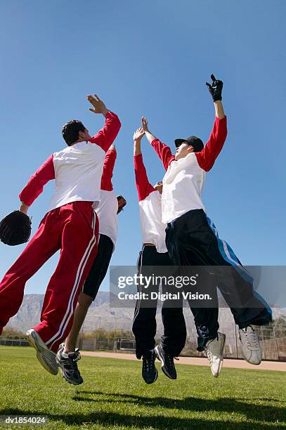 people in a baseball team jumping in a group giving each other a high five - baseballmannschaft stock-fotos und bilder