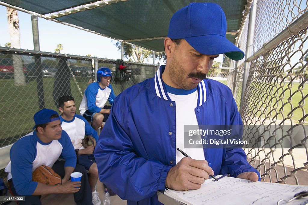 Sports Coach Writing on a Clipboard in a Dugout and Team Watching
