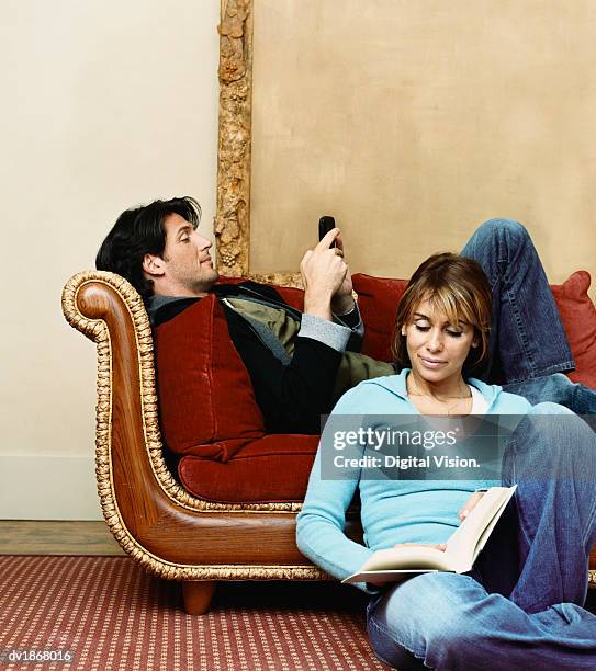 man on an ornate sofa texting on his mobile phone and his partner reading a book - ornate house furniture stock-fotos und bilder