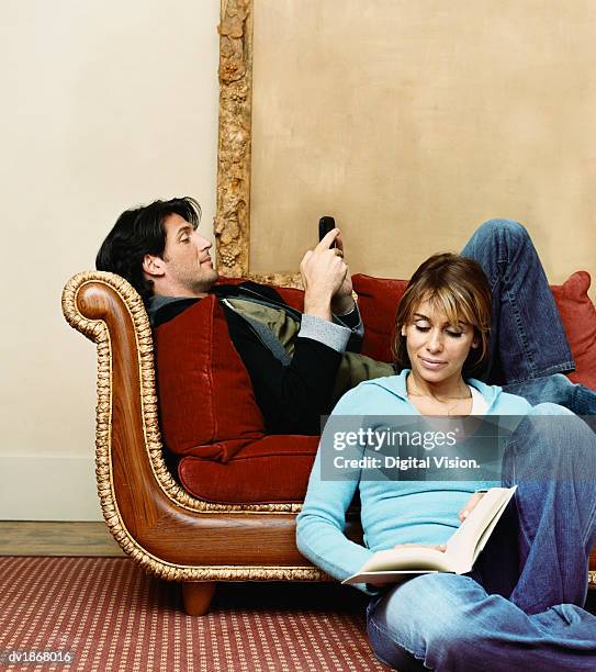 man on an ornate sofa texting on his mobile phone and his partner reading a book - pantalón decorado fotografías e imágenes de stock