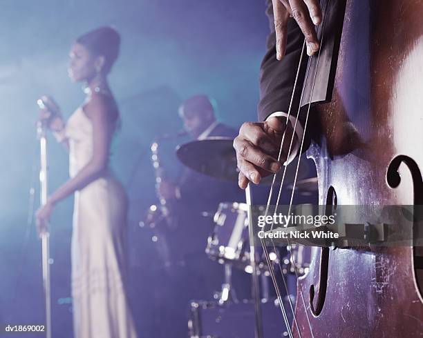 close-up of a man plucking a double bass on stage in a nightclub and a female singer and saxophonist standing in the background - ジャズ ストックフォトと画像