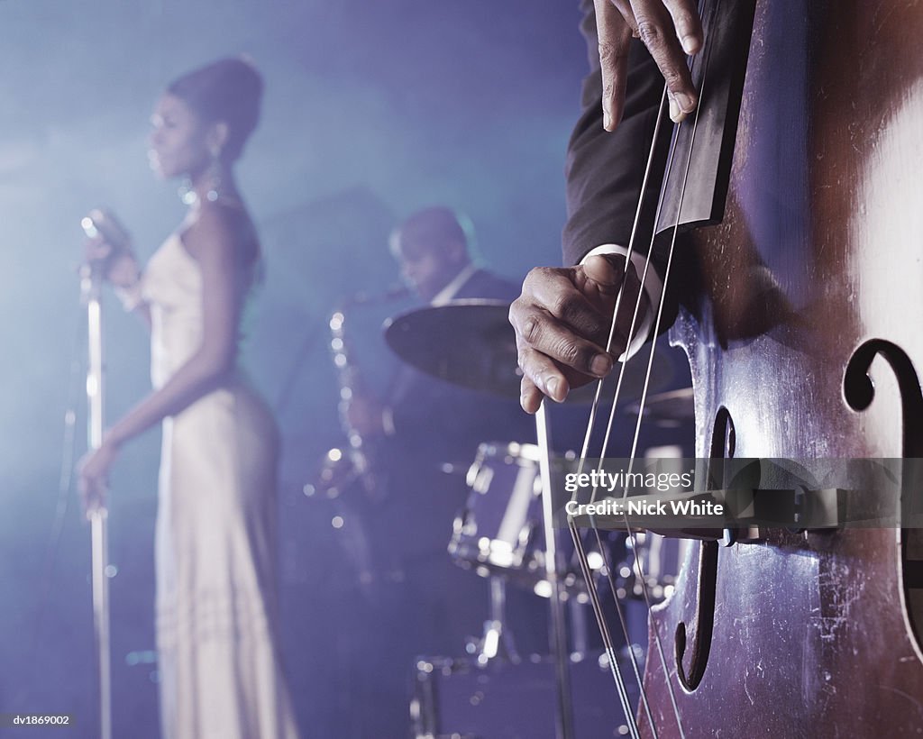 Close-up of a Man Plucking a Double Bass on Stage in a Nightclub and a Female Singer and Saxophonist Standing in the Background