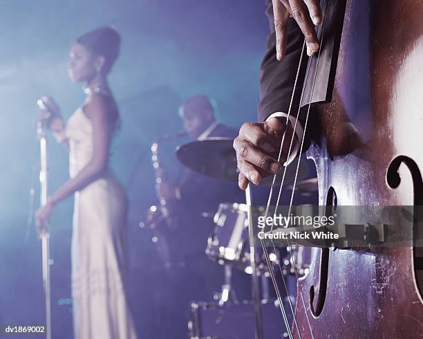 close-up of a man plucking a double bass on stage in a nightclub and a female singer and saxophonist standing in the background - club of former national players meeting stockfoto's en -beelden