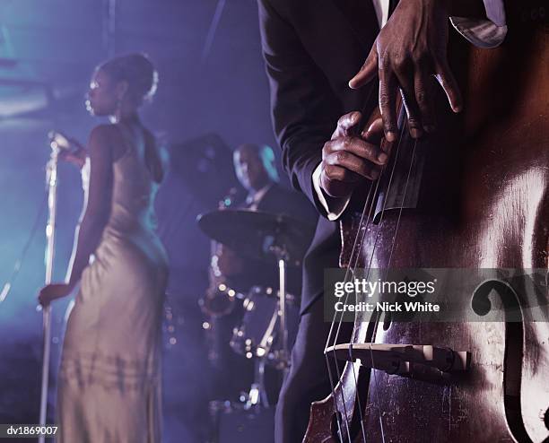 close-up of a man plucking a double bass on stage in a nightclub and a female singer and saxophonist standing in the background - bass drum stock-fotos und bilder
