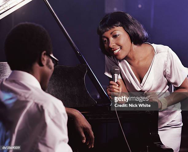 female singer in a nightclub holding a microphone and singing to a pianist - diva human role ストックフォトと画像