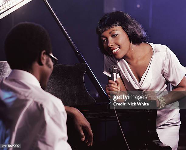 female singer in a nightclub holding a microphone and singing to a pianist - diva stock pictures, royalty-free photos & images