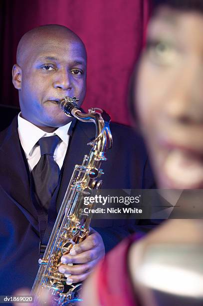 musician playing an alto saxophone in a jazz band standing behind a female vocalist - alto stock pictures, royalty-free photos & images