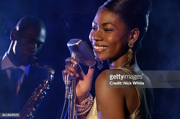 female jazz singer standing with a microphone in front of a man playing an alto saxophone - no alto stock-fotos und bilder