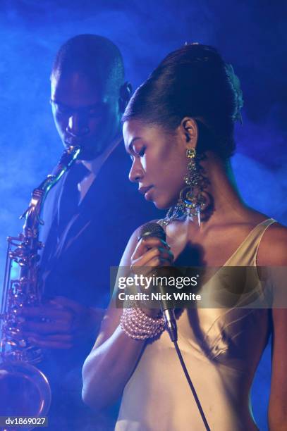 female jazz singer standing with a microphone in front of a man playing an alto saxophone - alto stock pictures, royalty-free photos & images