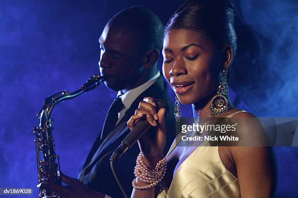 female jazz singer standing with a microphone in front of a man playing an alto saxophone - alto stock pictures, royalty-free photos & images