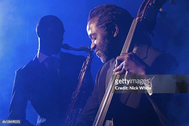 musician playing the double bass in front of a man playing an alto saxophone - jazz imagens e fotografias de stock