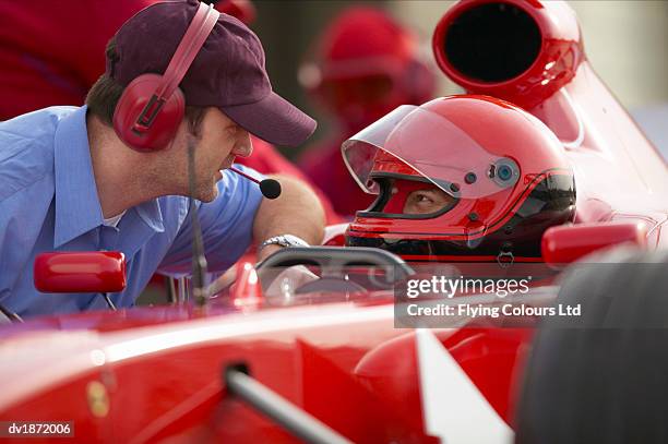 open-wheel single-seater racing car racing driver talking with a man wearing a headset during a pit stop - boxenstopp stock-fotos und bilder