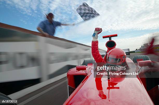 open-wheel single-seater racing car driver raising his fist in celebration as he passes a man waving a chequered flag - モータースポーツ ストックフォトと画像