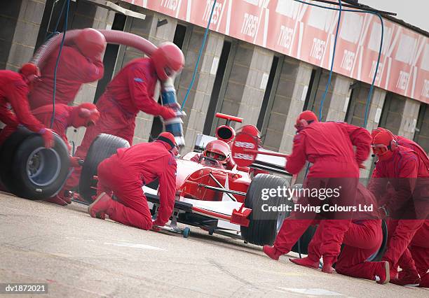 mechanics maintaining a red open-wheel single-seater racing car car at a pit stop - pit stop stock pictures, royalty-free photos & images