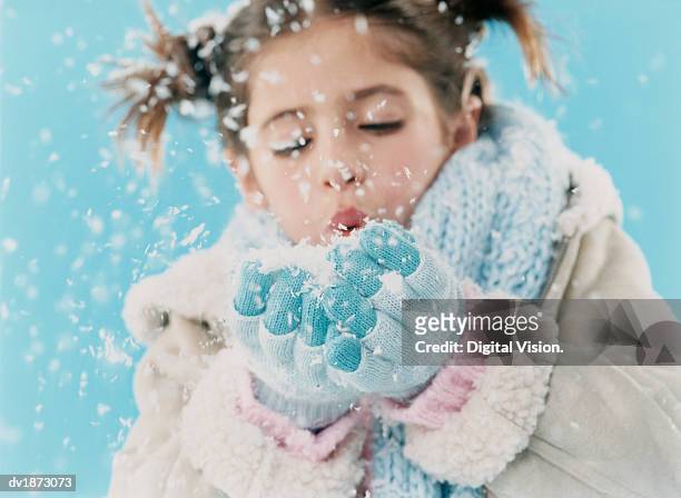 young girl wearing warm clothing and blowing a handful of snow - schnee pusten stock-fotos und bilder
