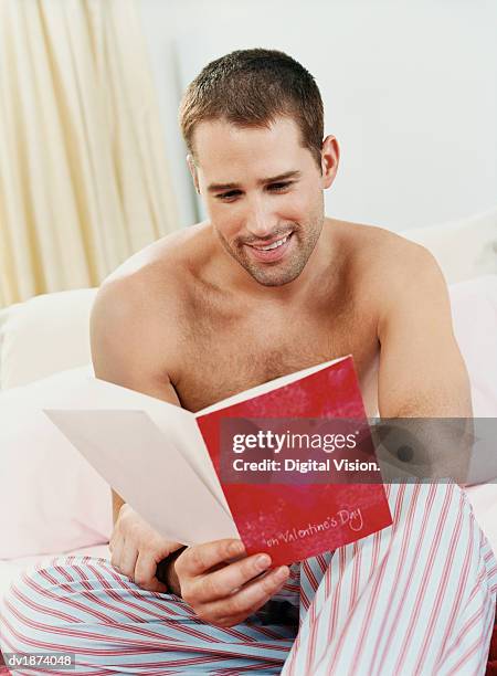 man wearing pajamas sitting in bed reading a valentines card - man reading card stock pictures, royalty-free photos & images
