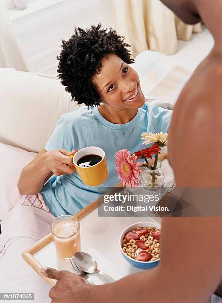 woman holding a mug of coffee and gazing at a man who has brought her breakfast in bed - brought stock pictures, royalty-free photos & images