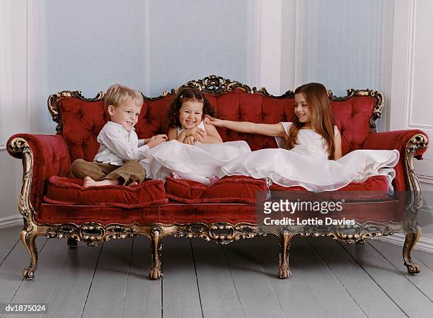 three well dressed young girls and young boy sit on an ornate sofa, one of the girls being tickled - ornate house furniture stock-fotos und bilder