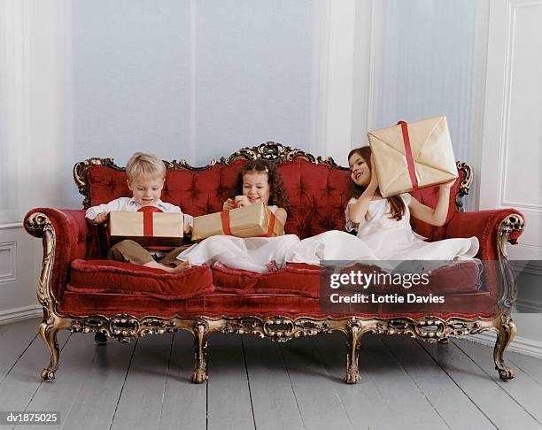 well dressed young boy and young girls sit on an ornate sofa excitedly unwrapping gifts - ornate house furniture stock-fotos und bilder